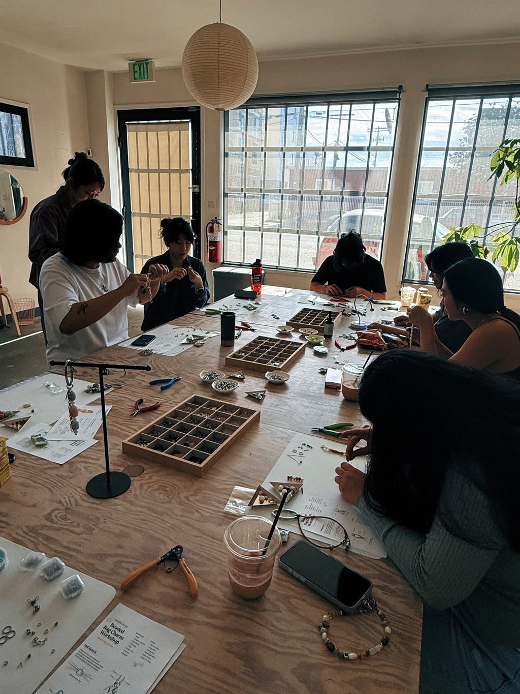 Group of people working on craft projects at a table with various materials and tools.