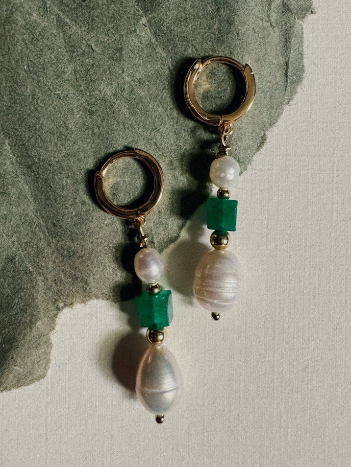 Pair of earrings with green and clear beads on a stone surface