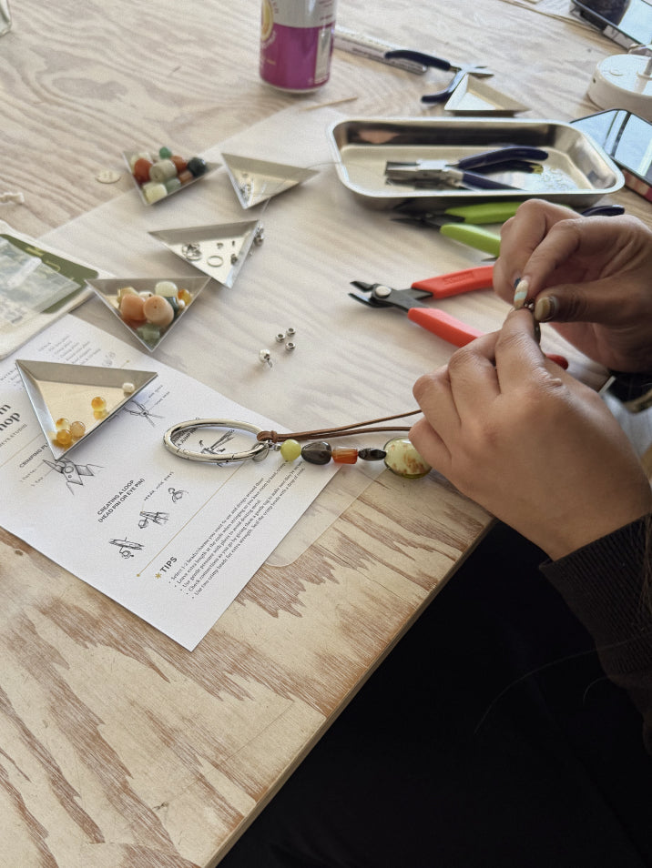 Person crafting a keychain with beads on a wooden table.