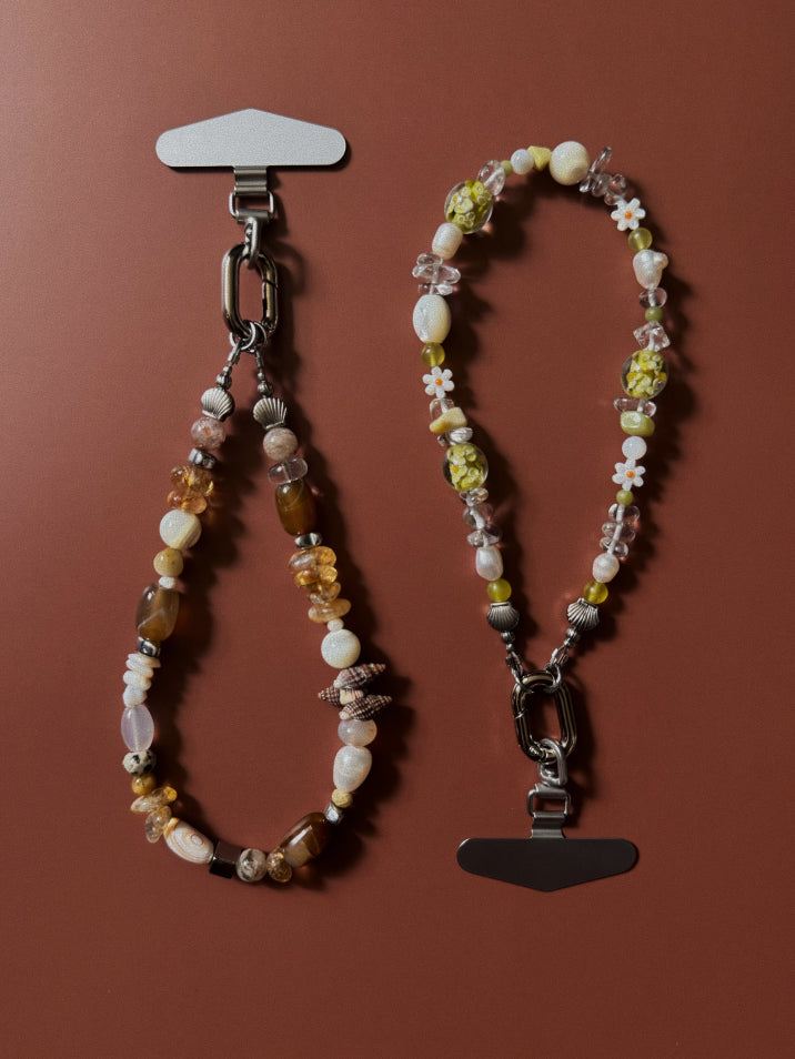 Two beaded phone wristlets against a brown background