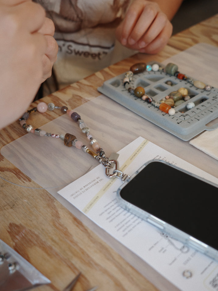 Close-up of hands working on a beaded bracelet with tools and materials on a wooden table.
